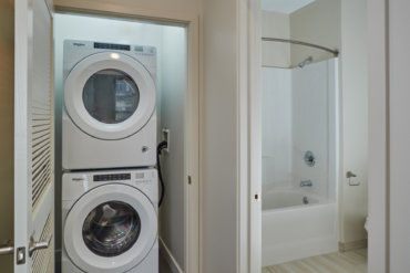 View into the full bath and laundry room with stackable washer and dryer in apartment 1-B.