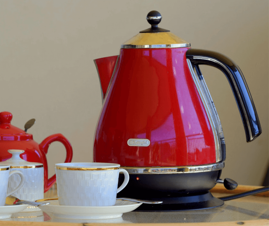 Red electric tea kettle sitting beside two tea cups. Image: John Finklestein