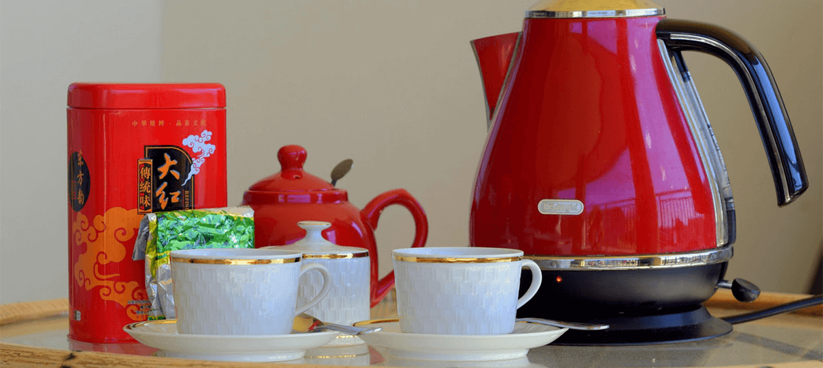 Red electric tea kettle sitting beside two tea cups. Image: John Finklestein