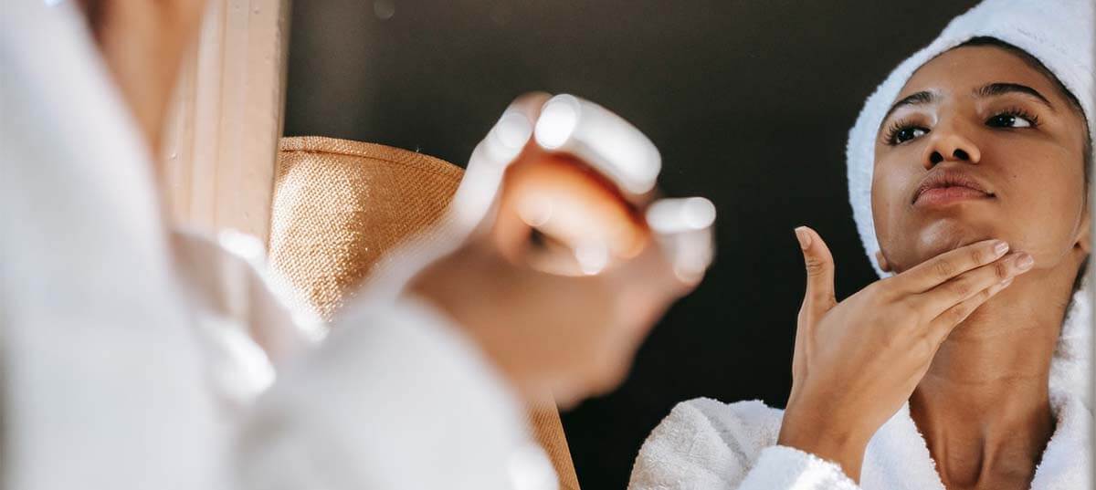 Woman wearing a bathrobe and hair towel applying a moisturizer. Image credit: Sora Shimazaki 