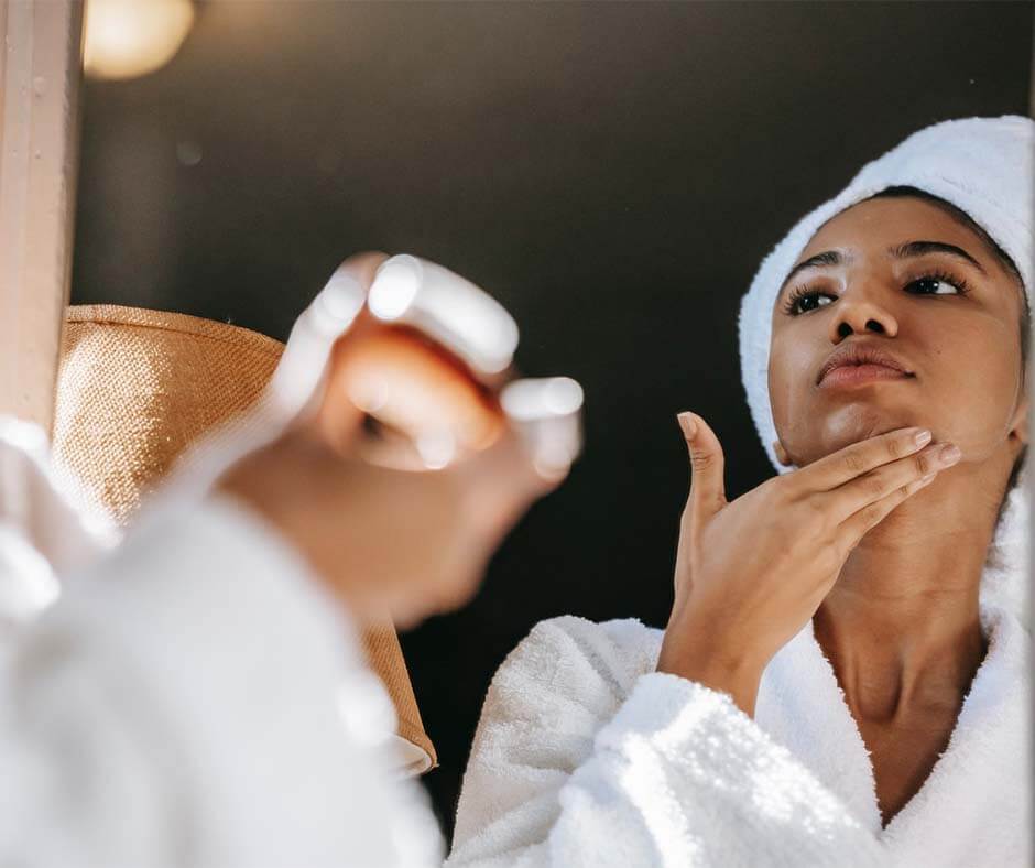 Woman wearing a bathrobe and hair towel applying a moisturizer. Image credit: Sora Shimazaki