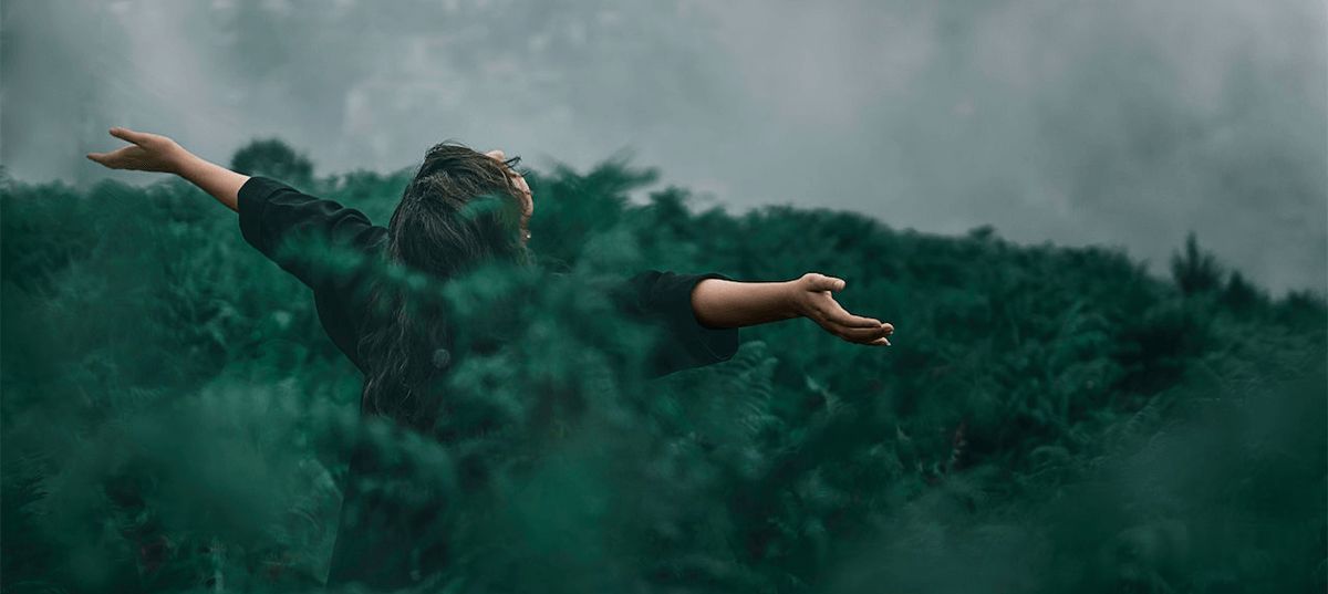 Person standing in a grass field with their arms raised. Image credit: Kourosh Qaffari 