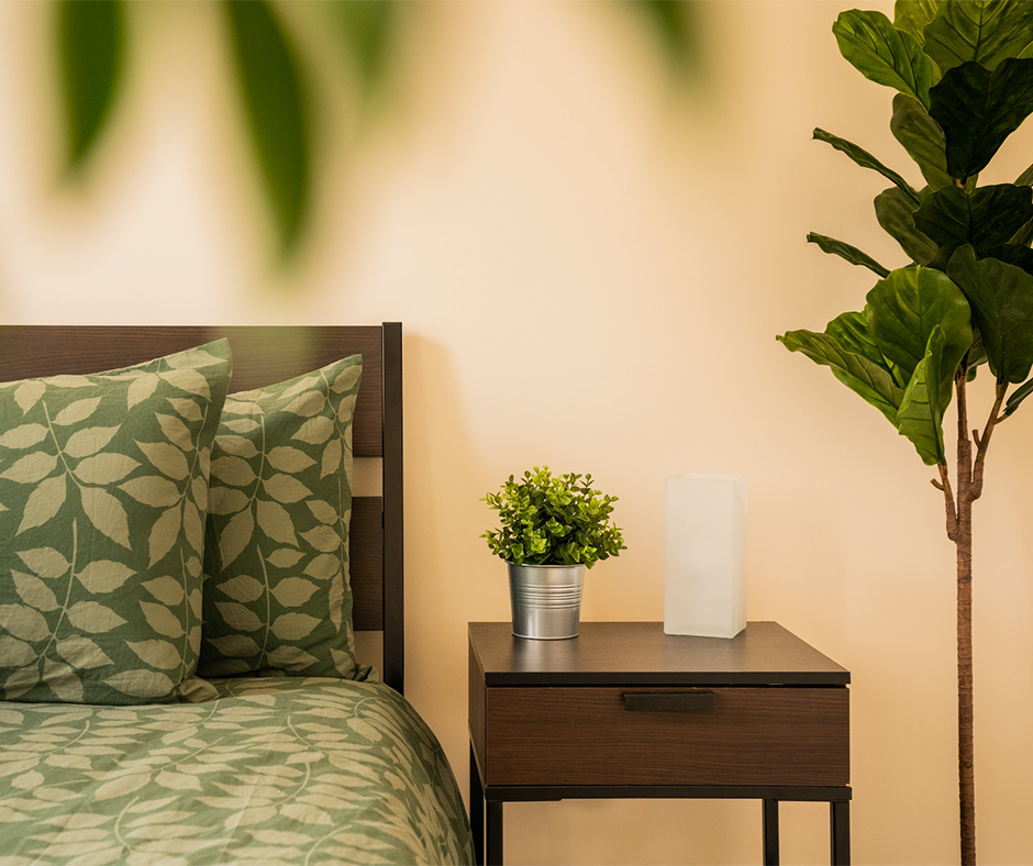Bedroom with houseplants, wood furniture, and leaf-patterned bedding.