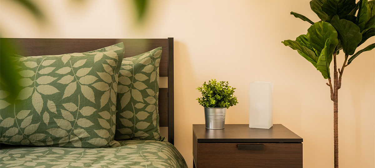 Bedroom with houseplants, wood furniture, and leaf-patterned bedding.